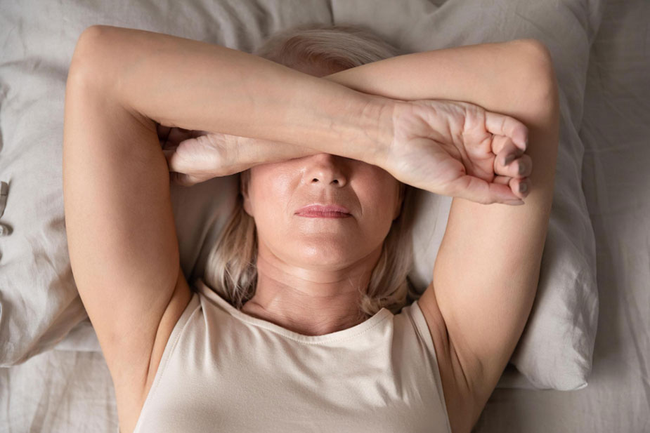 Žena u srednjim godinama pati od vrućine, što je simptom menopauze. Drži ruku na čelu i pravi grimasu od neprijatnosti.