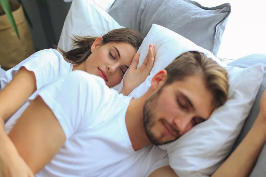 Par spava mirno, žena postavlja ruku na uho dok muškarac spava bez hrkanja