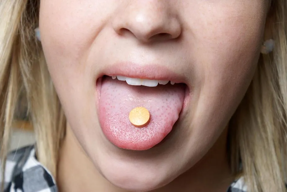 Žena drži tabletu bez šećera na jeziku za suva usta.